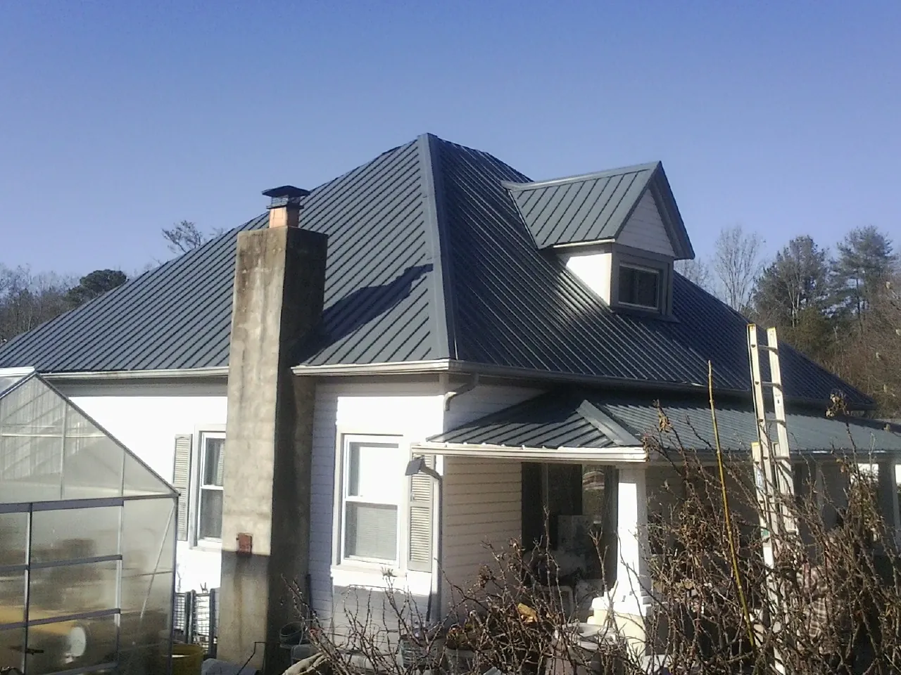 Dark blue standing seam metal roof on a white farmhouse with dormer — Slate & Tile Roof Repair by Roofing Brothers in East Bethany