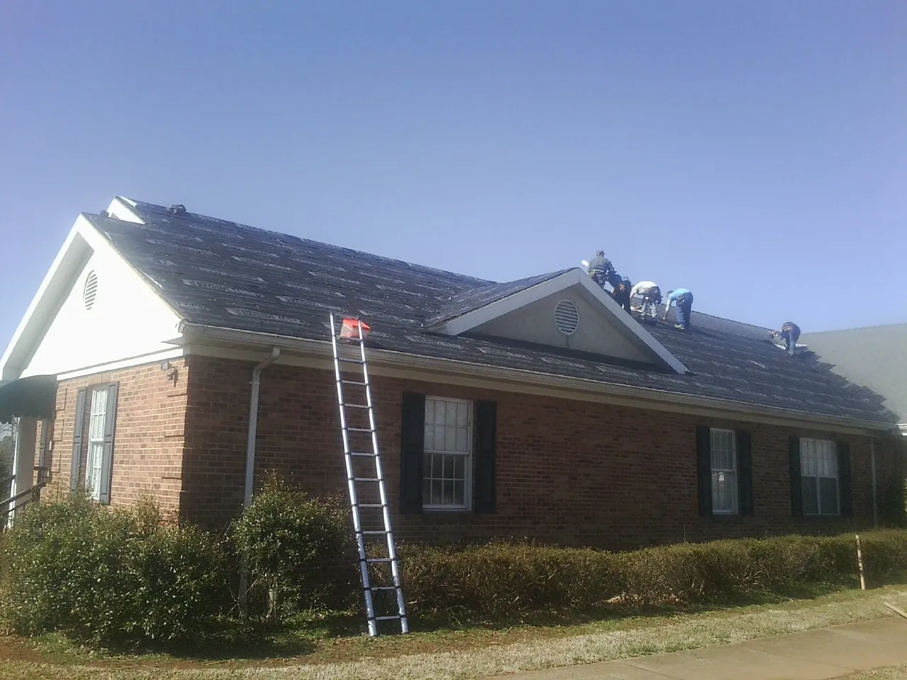 Crew tearing shingles off a brick ranch roof with a ladder set — Metal Roof Repair work by our crew in East Bethany