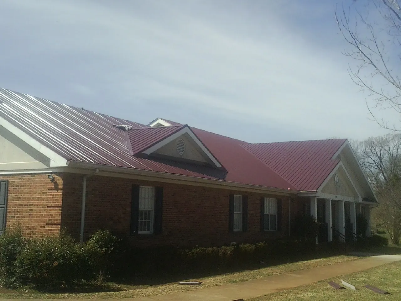 Red metal roof with gabled entries on a long brick building, from a Hail Damage Roof Repair job in East Bethany