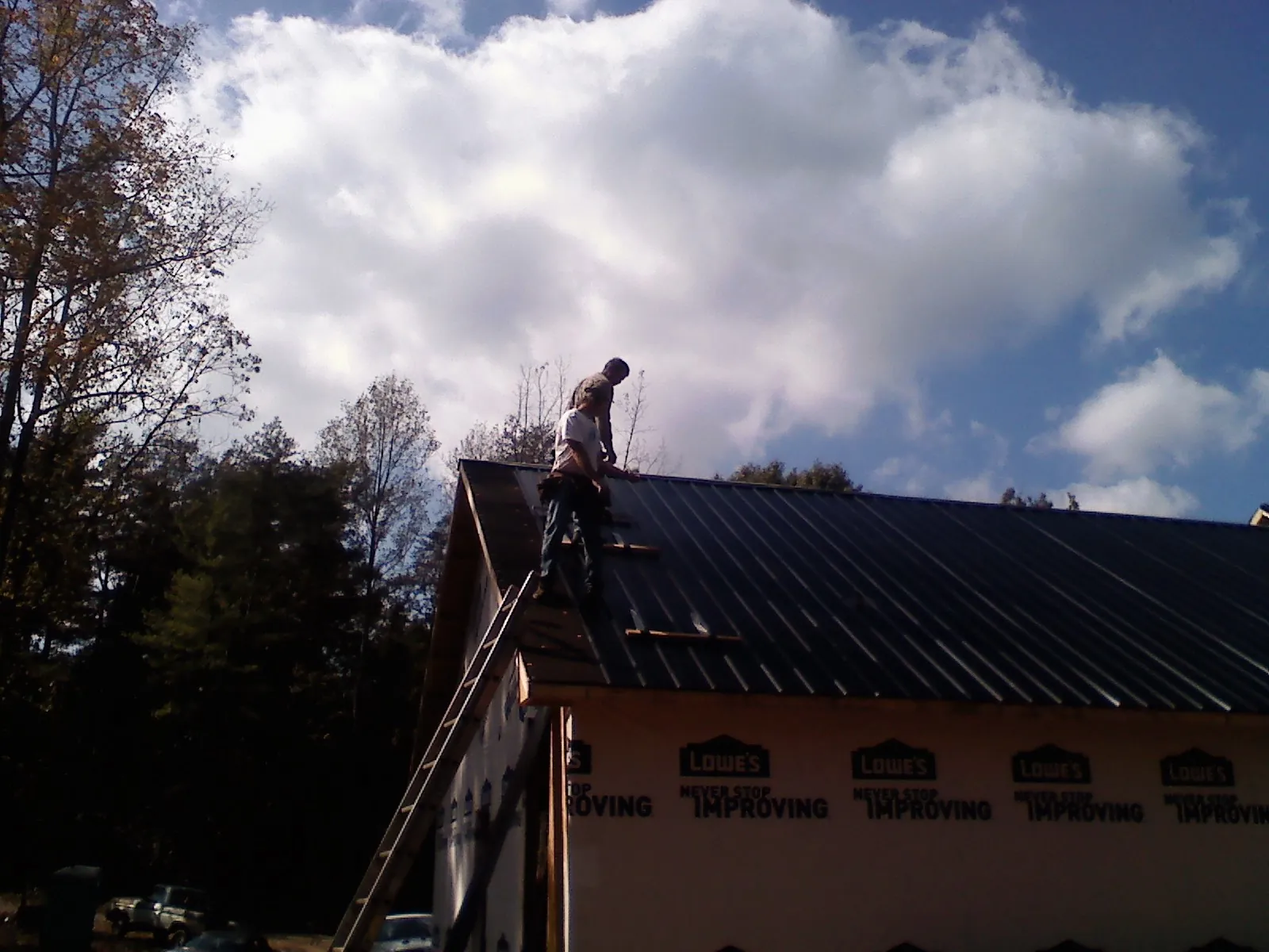 Roofer fastening dark metal panels high against a cloudy sky, from a Roof Inspection job in East Bethany