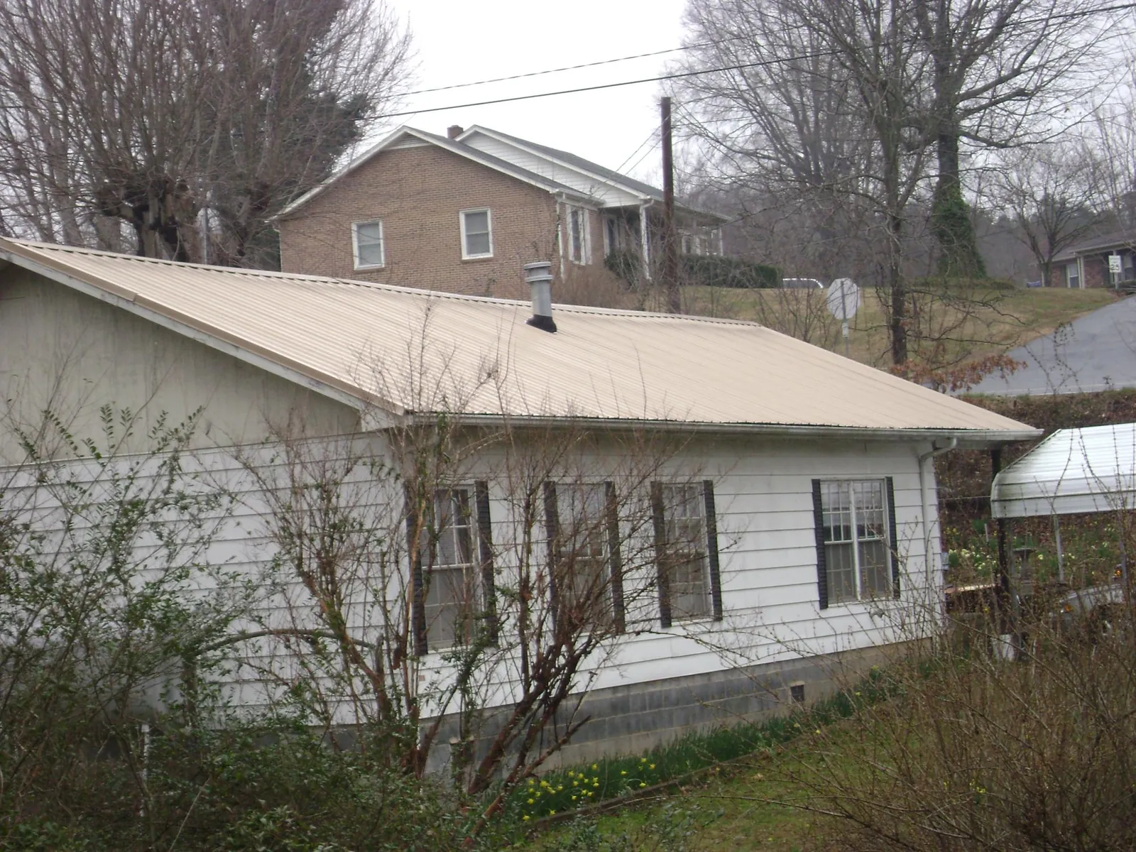 Tan metal roof on a white sided house set into a hillside — Commercial Roofing by Roofing Brothers in East Bethany